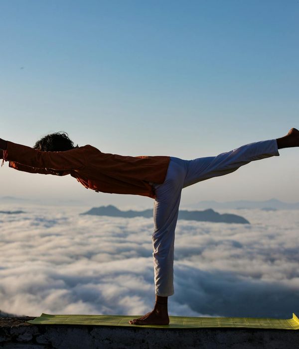Silhouette of a person in a powerful yoga warrior pose at sunrise.